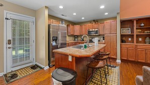 A kitchen with wooden cabinets, stainless steel appliances, and a central island with stools. - A Luxury Plus Level Hideout (PIGEON FORGE)