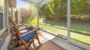 A covered patio with two wooden rocking chairs, a stone wall, and a view of a green lawn and trees. - A Luxury Plus Level Hideout (PIGEON FORGE)