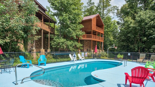 Un área de piscina con terraza de madera, sillas de descanso y valla alrededor.