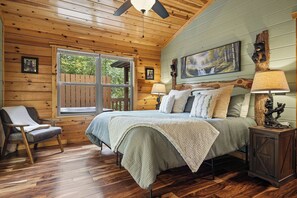 A cozy cabin-style bedroom with a bed, a chair, a nightstand, and a window.