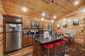 A wooden cabin interior with a kitchen, bar area, and dining space.