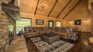 A cozy cabin interior with a sectional sofa, a fireplace, wooden walls, and a chandelier. - If Every View Could Be This Perfect (GATLINBURG)