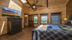 A wooden cabin bedroom with a bed, a dresser, a ceiling fan, and a painting of a landscape. - If Every View Could Be This Perfect (GATLINBURG)