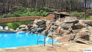 A swimming pool with a rocky edge, a wooden deck, and a small cabin in the background. - If Every View Could Be This Perfect (GATLINBURG)