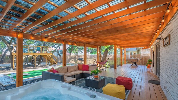 A covered outdoor area with a hot tub, seating, and a wooden deck. - Hot Tub, Unique Tree Deck & Game Room near Six Flags Fiesta Texas (San Antonio)