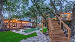 A backyard with a wooden deck, a hammock, and a covered seating area with string lights. - Hot Tub, Unique Tree Deck & Game Room near Six Flags Fiesta Texas (San Antonio)