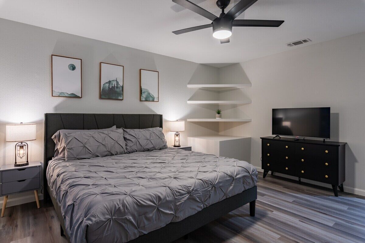A modern bedroom with a bed, nightstands, a TV, and a ceiling fan.
