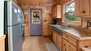 A compact kitchen with wooden walls, a refrigerator, a sink, and a window. - Taking Hide And Go Seek To The Next Level (PIGEON FORGE)