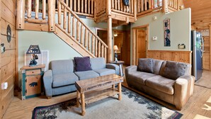 A cozy living room with a wooden staircase, two sofas, a coffee table, and a patterned rug. - Taking Hide And Go Seek To The Next Level (PIGEON FORGE)