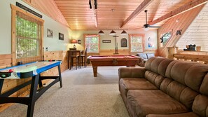 Una habitación acogedora con mesa de billar, un sofá de cuero marrón y techo de madera.