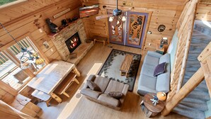 A cozy cabin interior with a stone fireplace, wooden furniture, and a large window. - Taking Hide And Go Seek To The Next Level (PIGEON FORGE)