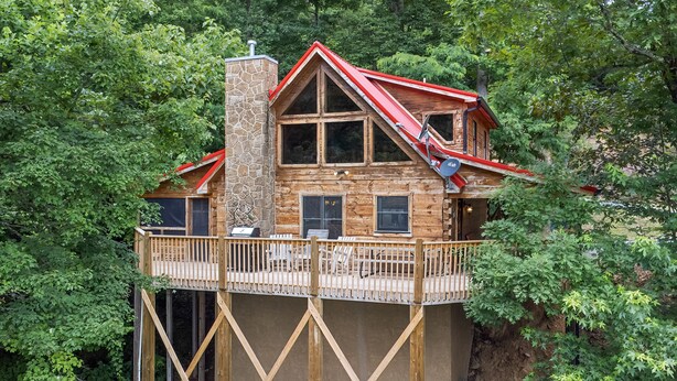 A wooden cabin with a balcony, surrounded by dense trees. - Taking Hide And Go Seek To The Next Level (PIGEON FORGE)