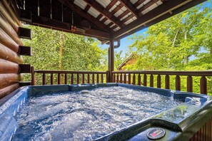 Un bain à remous sous une pergola en bois, avec vue sur les arbres et une maison en arrière-plan.