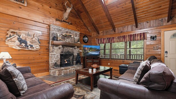 A cozy cabin interior with a stone fireplace, leather sofas, and a television. - Experience Joy From A Hot Tub In The Mountain Air (PIGEON FORGE)