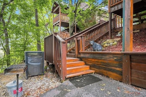 Un escalier en bois mène à une terrasse ornée d’une statue d’ours, le tout étant entouré d’arbres.