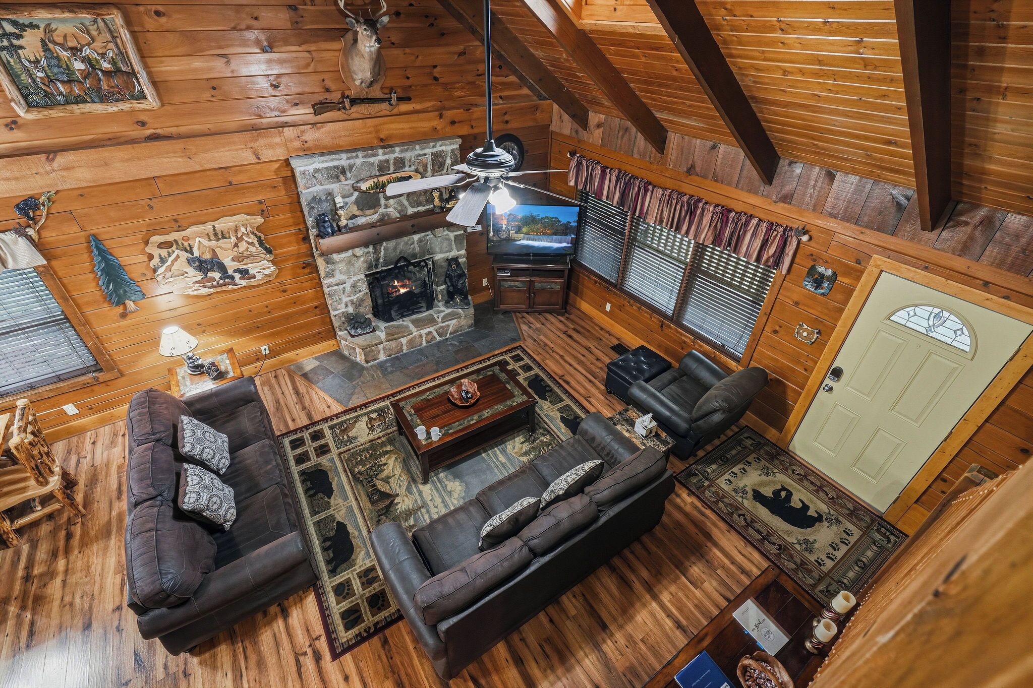 A cozy cabin interior with a stone fireplace, leather sofas, and a television.