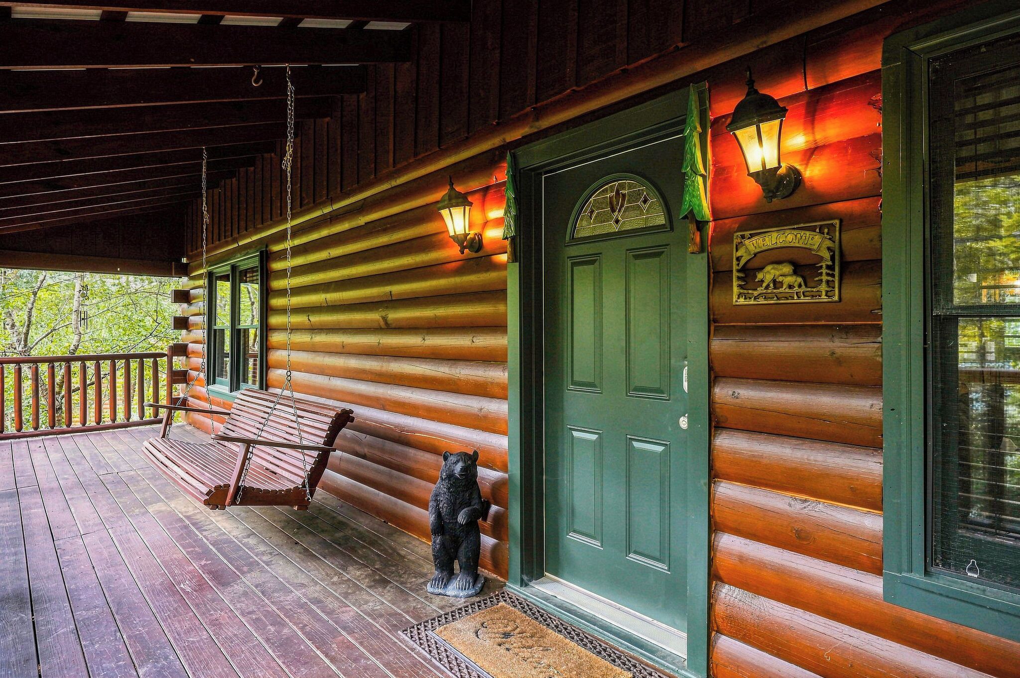 Eine Holzhütte mit Veranda, einer grünen Tür und einer Bärenstatue.