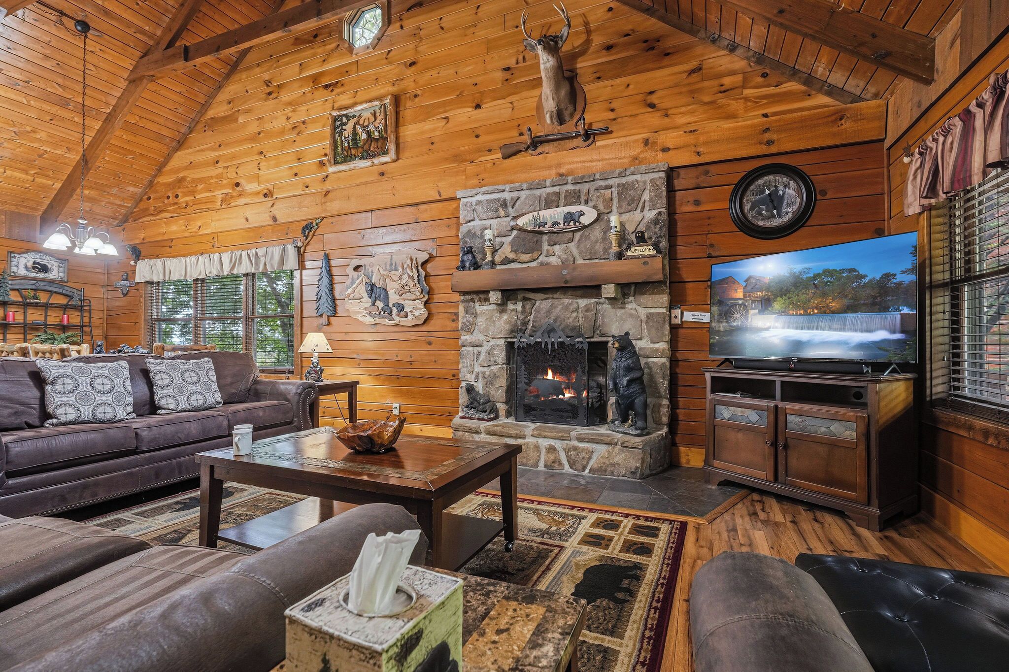 A cozy log cabin interior with a stone fireplace, leather furniture, and a television.