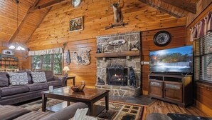 Interior acogedor de una cabaña de madera con chimenea de piedra, muebles de cuero y una televisión.