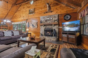Interior acogedor de una cabaña de madera con chimenea de piedra, muebles de cuero y una televisión.