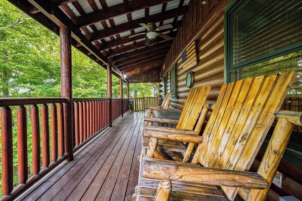 A wooden porch with a railing, a ceiling fan, and several wooden chairs.