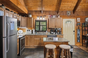 A cabin-style kitchen with wooden cabinets, a stainless steel refrigerator, a built-in oven, a sink, and a window with blinds.