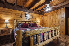 A wooden bedroom with a bed, a ceiling fan, and wooden walls.