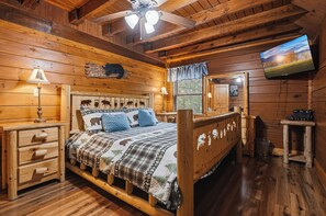 Une chambre à coucher dans un chalet en bois, avec un lit, des tables de chevet, une télévision et une fenêtre donnant sur un paysage agréable.