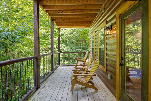 A wooden deck with four Adirondack chairs, a railing, and a door leading to a covered porch.