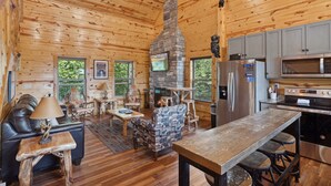 L’intérieur d’un chalet en bois comprend une cheminée en pierre, un coin repas, une cuisine équipée d’appareils modernes et un espace salon confortable.