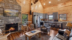 Un intérieur de chalet chaleureux avec une cheminée en pierre, des murs en bois, un coin cuisine et un espace repas.