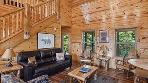 L’intérieur d’un chalet en bois comprend un escalier, un canapé en cuir noir, une table à manger et des chaises.