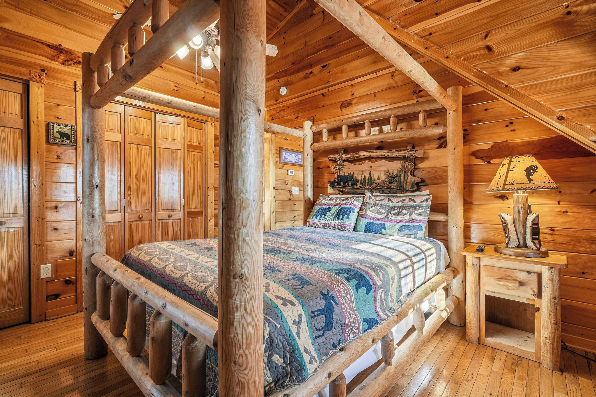 Dormitorio tipo cabaña de troncos con cama de dos plazas, paredes de madera y ventilador de techo.