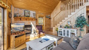 A cozy cabin interior with a fireplace, wooden walls, a staircase, and a television in the living area. - Get Away From The Grind For Some Tlc (PIGEON FORGE)