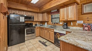 A kitchen with wooden cabinets, stainless steel appliances, and a granite countertop. - Get Away From The Grind For Some Tlc (PIGEON FORGE)