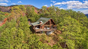 A cabin with a deck, surrounded by dense forest and a mountain backdrop. - Get Away From The Grind For Some Tlc (PIGEON FORGE)