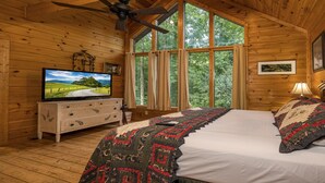 A cabin room with a bed, a television on a dresser, a ceiling fan, and large windows with curtains. - Accessible (Not ADA)*Gatlinburg*Relaxing (SEVIERVILLE)