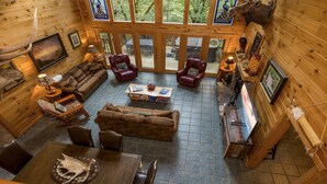 A cozy cabin interior with a wooden interior, a stone fireplace, and a large window overlooking a forest. - Accessible (Not ADA)*Gatlinburg*Relaxing (SEVIERVILLE)