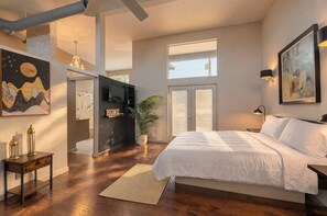 A modern bedroom with a large bed, a desk, a TV, and a plant. - Mid-Century Retreat with Private Pool near Airport, Pearl & Downtown (San Antonio)