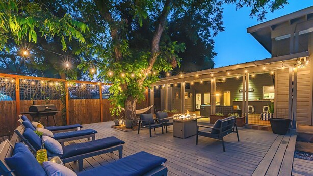 An outdoor deck with lounge chairs, a barbecue grill, string lights, and a fire pit. - Private Jetted POOL, Firepit & BBQ in a Stunning House By Airport (San Antonio)