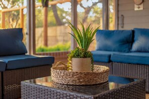 A wicker coffee table with a potted plant, a wicker chair, and a blue sofa with cushions.