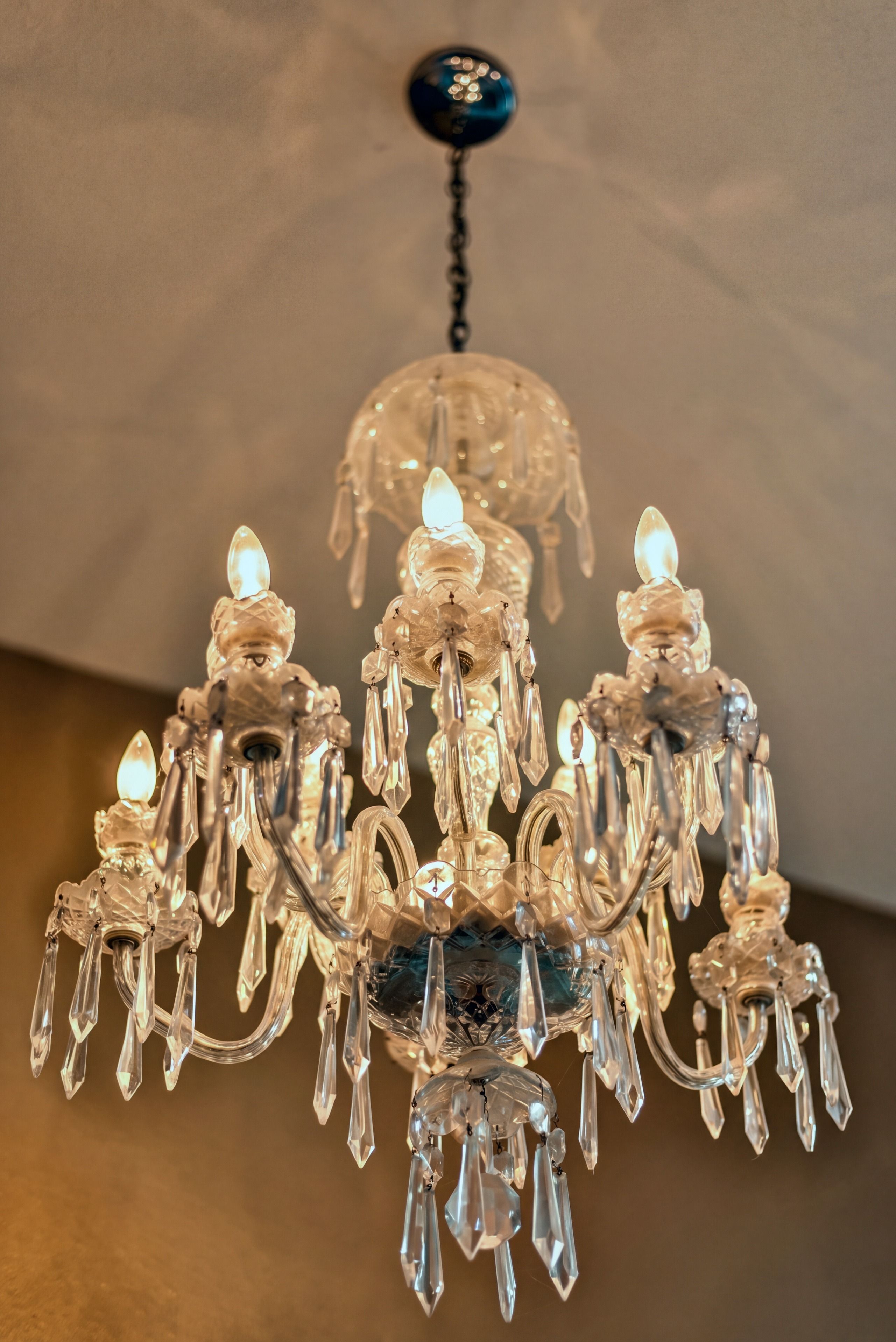 Un lustre doté de plusieurs bras et d’ampoules en cristal, suspendu à un élément fixé au plafond.