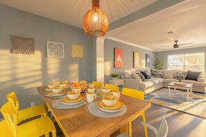 A modern living room with a dining area, featuring a wooden table, yellow chairs, and a ceiling fan. - Private Hot Tub & Game Room near SeaWorld and Lackland AFB (San Antonio)