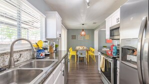 A modern kitchen with stainless steel appliances, a dining area with yellow chairs, and a view of the outdoors through large windows. - Private Hot Tub & Game Room near SeaWorld and Lackland AFB (San Antonio)