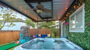 A hot tub under a covered patio with a ceiling fan, a wooden fence, and a green wall with climbing plants. - Private Hot Tub & Game Room near SeaWorld and Lackland AFB (San Antonio)