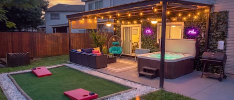 A backyard with a hot tub, fire pit, outdoor seating, and string lights.