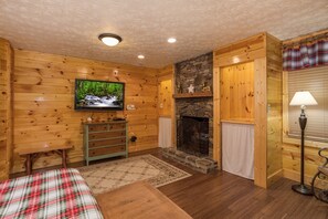 A cozy log cabin interior with a stone fireplace, wooden walls, a television, and a plaid-patterned bed. - Pigeon Forge*ZERO Stairs*Sleeps 10 (PIGEON FORGE)