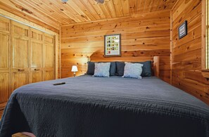 A wooden-paneled room with a bed, pillows, a nightstand, and a framed menu on the wall. - Pigeon Forge*Romantic*Cozy*Great for Couples (PIGEON FORGE)