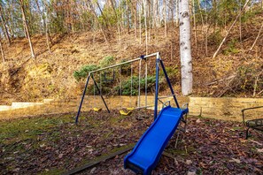 Ein Spielplatz mit einer blauen Rutsche, Schaukeln und einer Ziegelmauer.
