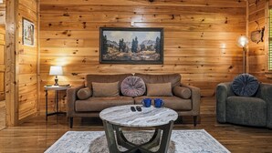 A cozy cabin interior with a wooden interior, a sofa, a coffee table, and a painting on the wall. - Pigeon Forge*Romantic*Cozy*Great for Couples (PIGEON FORGE)
